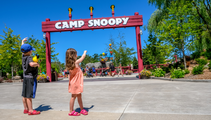 a young boy and girl face, and point toward, entrance to Camp Snoopy at Michigan's Adventure