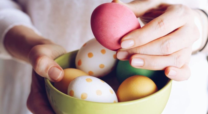 Hands holding a green bowl full of polka dot and colored Easter Eggs