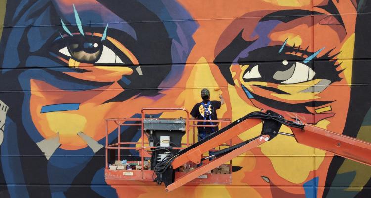 Image of artist on lift painting a mural of an African-American child's eyes.