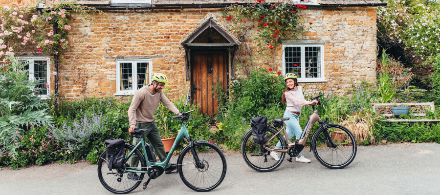 Couple on E bikes outside picturesque Kingham house