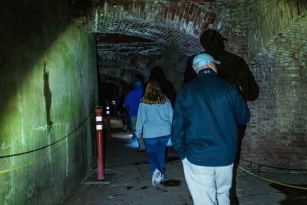 A man and woman walk through a dark, brick tunnel at Fort Delaware State Park during a Paranormal Tour.