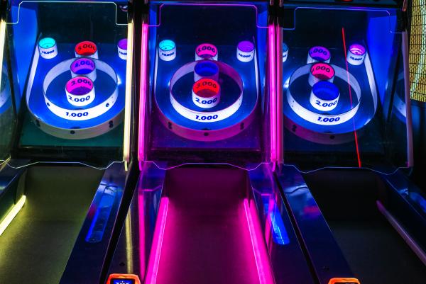 Three lanes of arcade bowling lit up in yellow, pink and blue lights