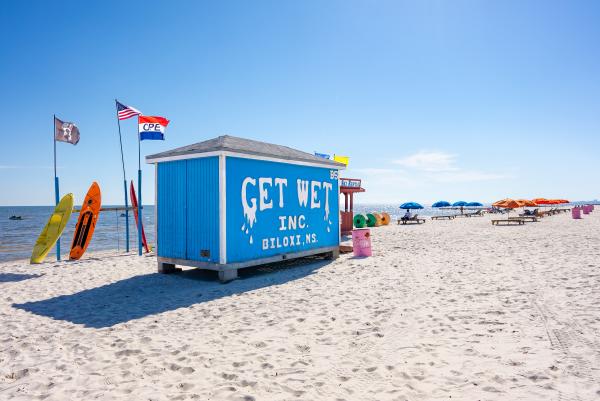 Blue Get Wet, Inc. Rental building on the beach surrounded by colorful rentals, such as kayaks and beach chairs.