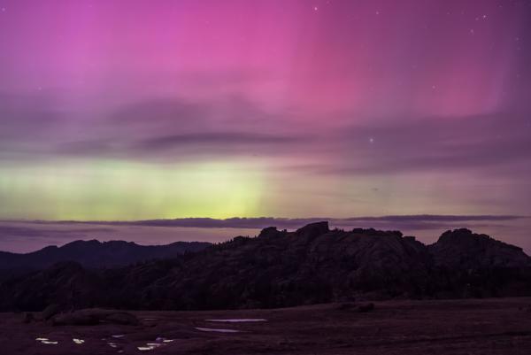 Purple and green northern lights over rocks
