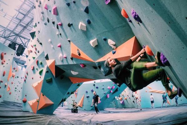 A female in the foreground climbs an indoor rock wall in a wide shot of the Minneapolis Bouldering Project