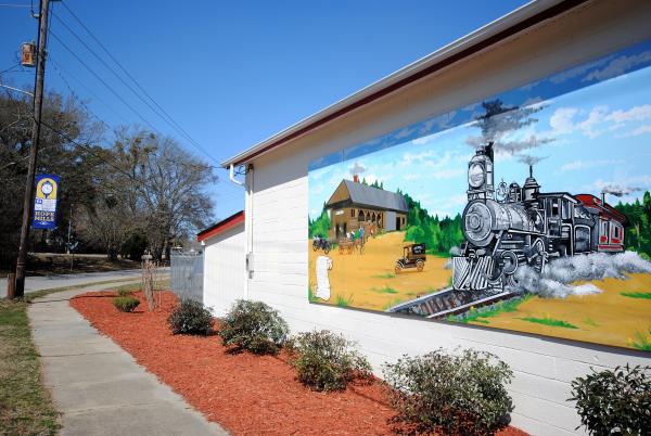 A mural of a steam engine train chugging through the countryside painted on the side of a Hope Mills, NC building