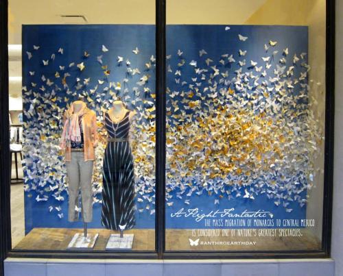 A storefront window with paper butterflies and some clothes on mannequins