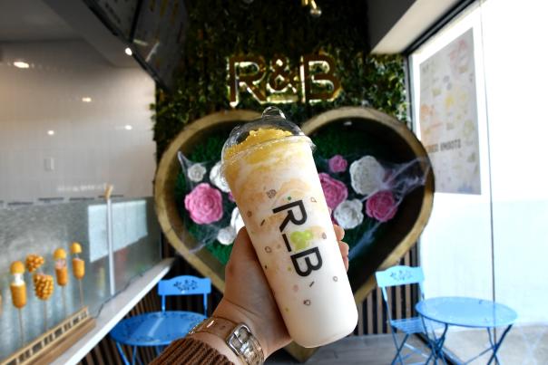milk boba being held in front of a grass wall with a heart