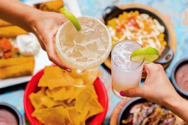 Two mixed drinks toasting over a plethera of tex-mex