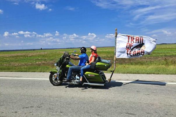 Trail of Tears Motorcycle Ride. Two people on a motorcycle with a Trail of Tears flag flying off the back.