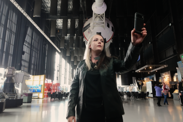Phoenyx Powell taking a selfie with the Saturn V rocket at the US Space and Rocket Center in the background.