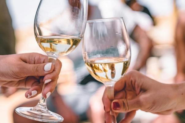 Two hands holding two glasses half filled with white wine coming together for a toast.