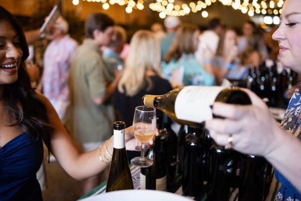 A smiling lady holds a glass while wine from a bottle is poured into it. Photo credit Abraham Rowe Photography