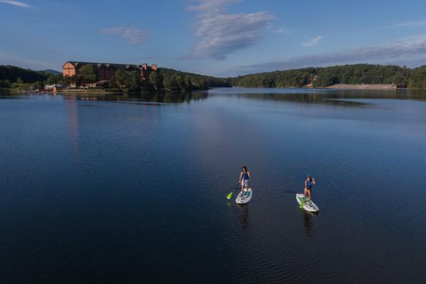 A male and female paddle on stand up paddle boards on a blue lake.