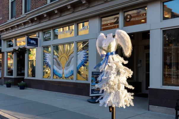 A parking meter is decorated with white tinsel and large white feathers to look like angel wings.