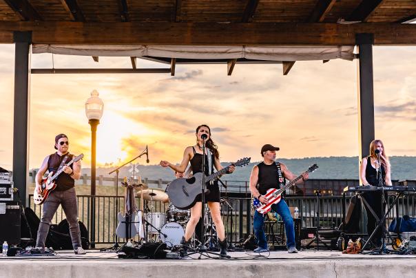 Female lead singer and her band perform at sunset on an open-air stage.