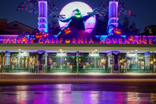 Image of the front of Disney California Adventure Park. Image is taken at night and a sign reading 'Disney California Adventure' is lit up in red and purple lights. Oogie Boogie from The NightMare Before Christmas is seen above the sign.