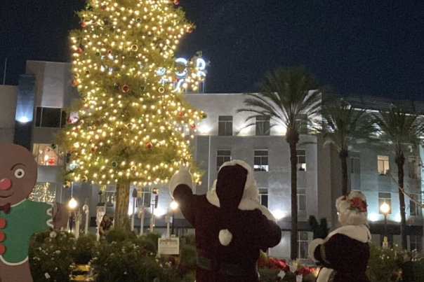 Image of Christmas tree lit up with Santa Claus and Mrs. Claus standing in front.