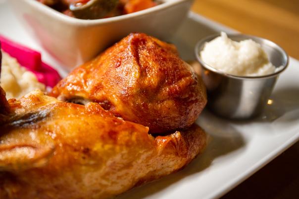 Image of chicken drumstick and chicken thigh served on a white plate with a small side of garlic sauce served in stainless steel metal container.