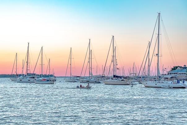 sailboats in a harbor with a sunrise in the background