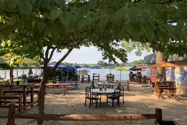 The Beach Bar MD with tables and chairs on their sandy beach by the water in Glen Burnie