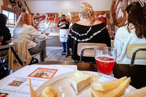 cheese plate and beer sit in front of camera during a cheesemaking workshop. the speaker presents to the audience.