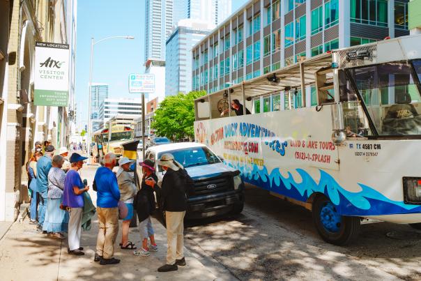 People line up on the sidewalk outside of the Austin Visitor Center waiting to board the Duck Tour vehicle