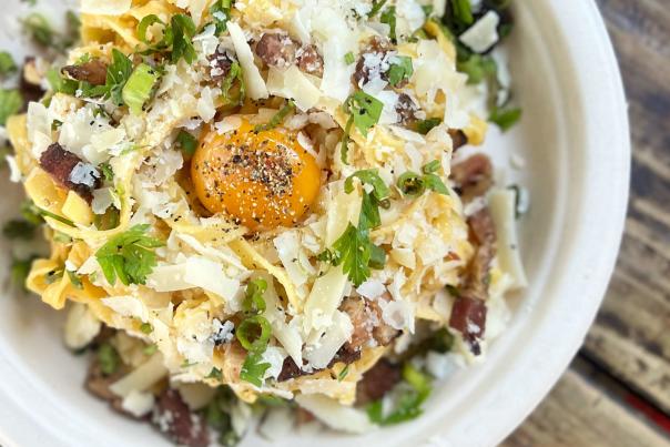 Heavy-duty paper plate on a wooden table, full of carbonara pasta.
