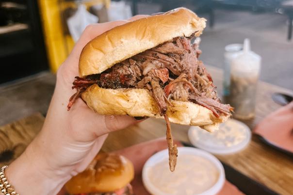 Hand holding a large barbecue sandwich close to the camera.