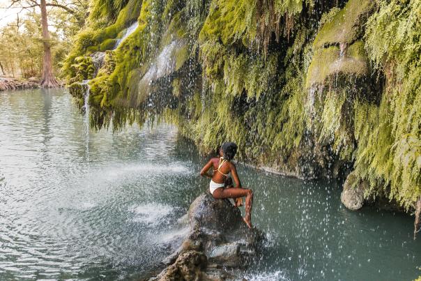 Woman sitting on a rock under waterfall at Krause Springs near Austin Texas