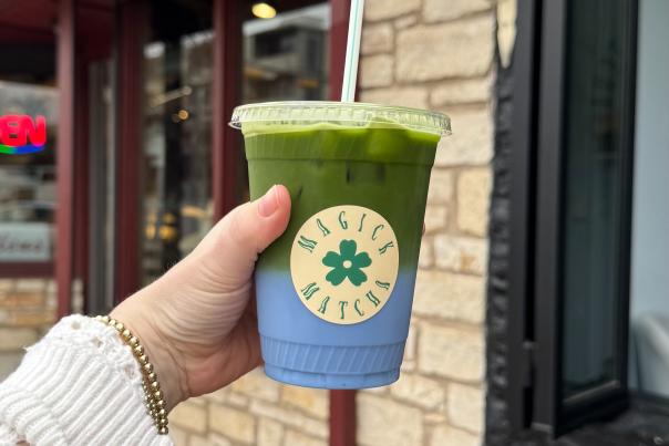Arm outstretched, holding a matcha latte layered with blue spirulina milk.