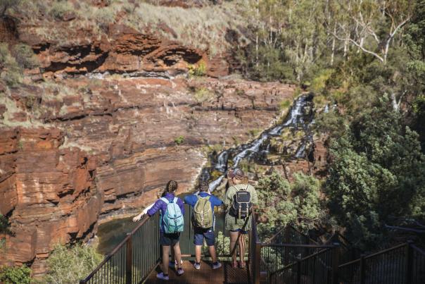 A mother and two children stand looking at Fortescue Waterfall from a lookout in Karijini National Park