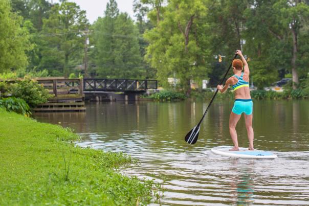 Woman Paddle Boarding With Bridge And Cars In Distance