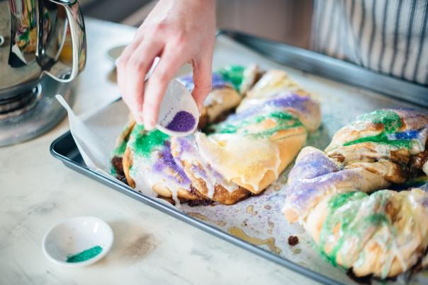 A baker decorates loaves of King Cake with the traditional purple and green Mardi Gras colors.