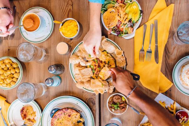 Top-down view of a table filled with food with two hands reaching for items on the table.