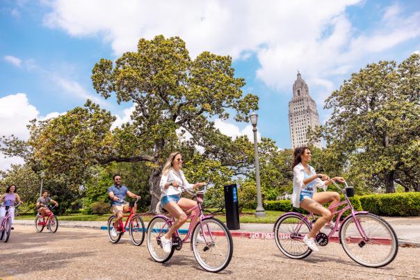 A group of five biking in Baton Rouge with the Louisiana State Capitol Building behind them.