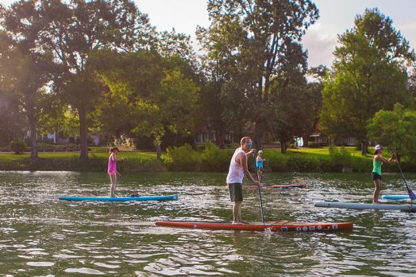 People stand-up paddle-boarding down peaceful river
