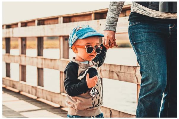 Little boy with sunglasses holding a Beaumont birdie holding a hand as he walks on the Cattail Marsh Boardwalk