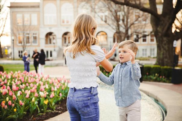 Two children play together at Bentonville City Square filled with blooming tulips, with a historic building in the background. The scene captures a lively outdoor atmosphere.