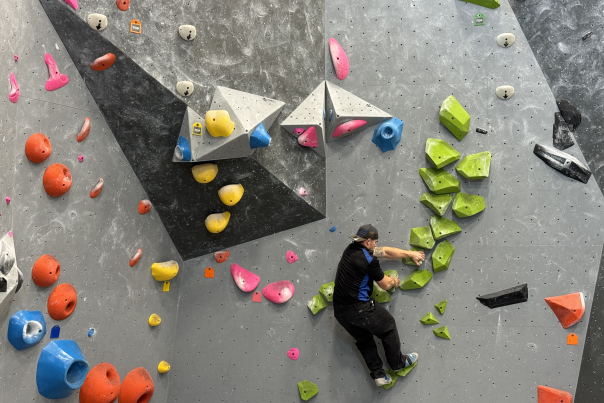 Climber scaling a bouldering wall at Climb Bentonville, featuring colorful handholds and challenging routes.