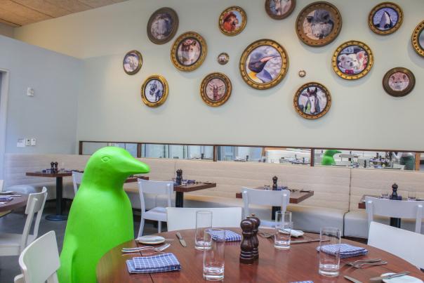 21C Penguin sitting at dinner table in front of art.