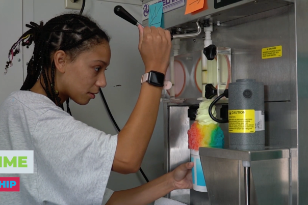 A person working a machine to put ice cream on top of a snow cone.