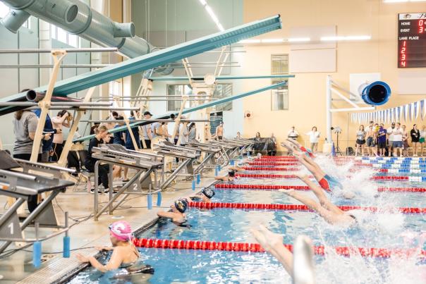 Swimmers dive into the pool at a competitive meet at Bentonville Community Center, showcasing athletic skill and precision in an exciting race.