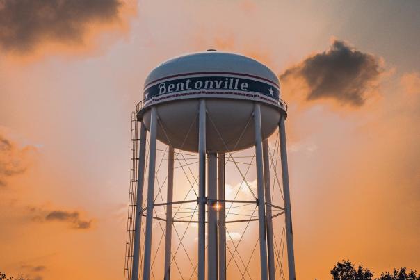 A Bentonville branded water tower with a bright orange sunset behind it.