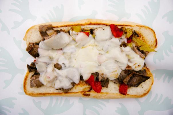 A hoagie bun open filled with slices of beef, peppers and onion topped with melted white cheese.