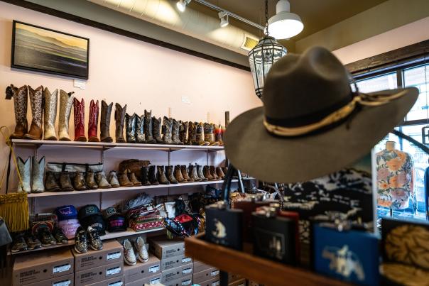 A display of various cowboy boots and hats in a boutique, with shelves lined with colorful footwear and accessories. A painting hangs above.
