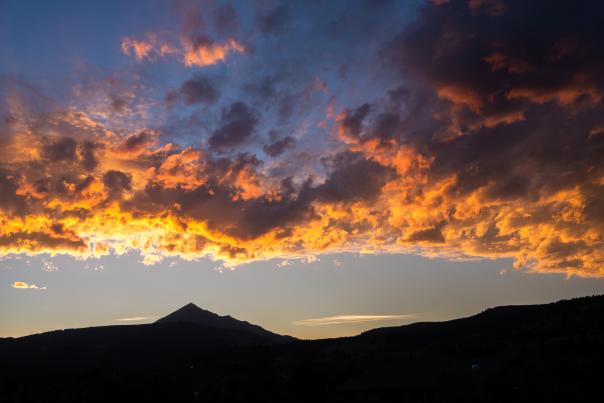 Vibrant sunset over a mountain silhouette, with dramatic clouds in shades of orange and purple, creating a stunning natural landscape.