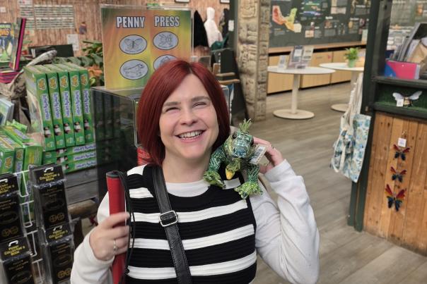 Sassy in the Butterfly Farm gift shop, she has a stuffed iguana on her shoulder smiling towards the camera