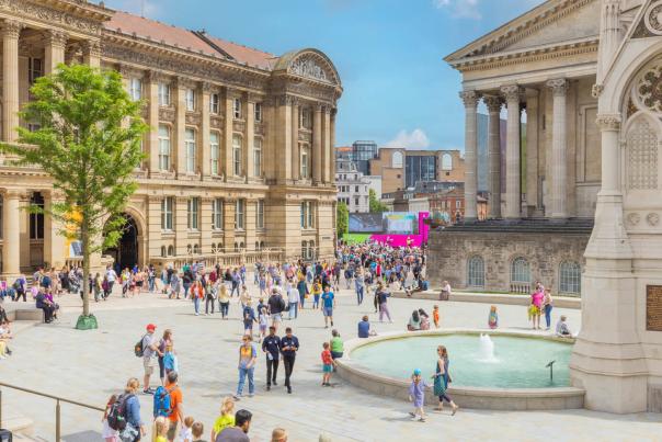 Groups of people sitting outside in summer clothes. Surrounded by Chamberlain Square fountain and Birmingham Museum and Art Gallery