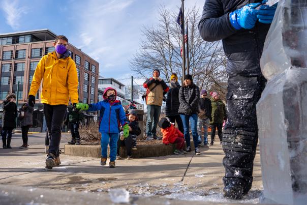 A dad holding his small son's hand as they approach a live carving demonstration during Freezefest